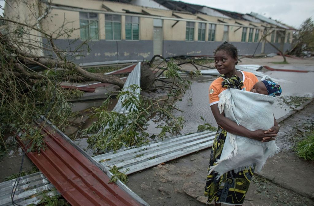 Eine Frau steht nach dem Sturm „Idai“ in Inhamizua mit einem Baby asuf dem Arm zwischen Trümmerteilen und umgekippten Bäumen.