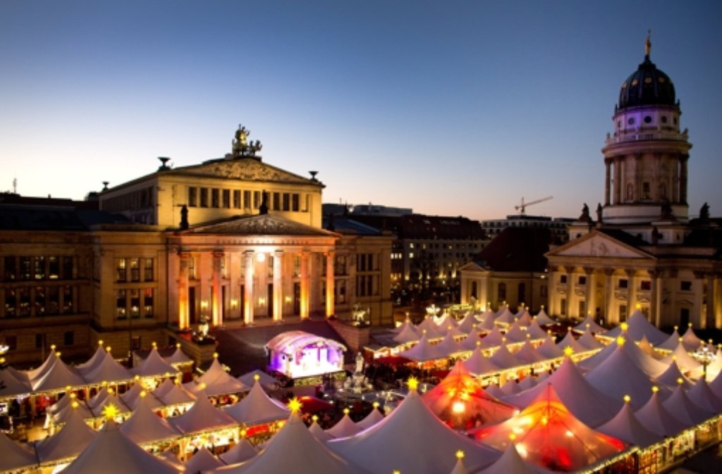 Hell erleuchtet sind die Stände auf dem Weihnachtsmarkt auf dem Gendarmenmarkt in Berlin. Im Hintergrund sind das Konzerthaus (M) und der Französische Dom (r) zu sehen.
