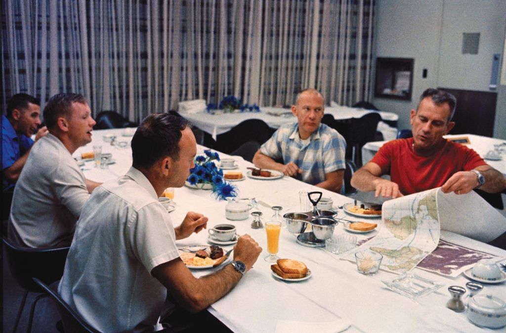Toast, Speck und Eier: Das Frühstück am Morgen des Starts von Apollo 11 fiel üppig und typisch amerikanisch aus. Aber selbst hier bleiben die Astronauten von Arbeit nicht verschont – was ebenfalls typisch war. Flugdirektor Donald Slayton geht den Flug mit ihnen durch.