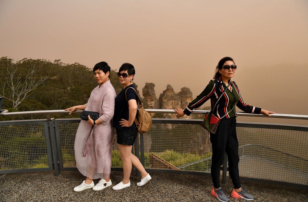 Seit Tagen wüten Buschfeuer im Osten Australiens: Das beeinträchtigt auch Urlauber, wie diese drei Touristinnen am Aussichtspunkt „Three Sisters“. Foto: dpa/Joel Carrett