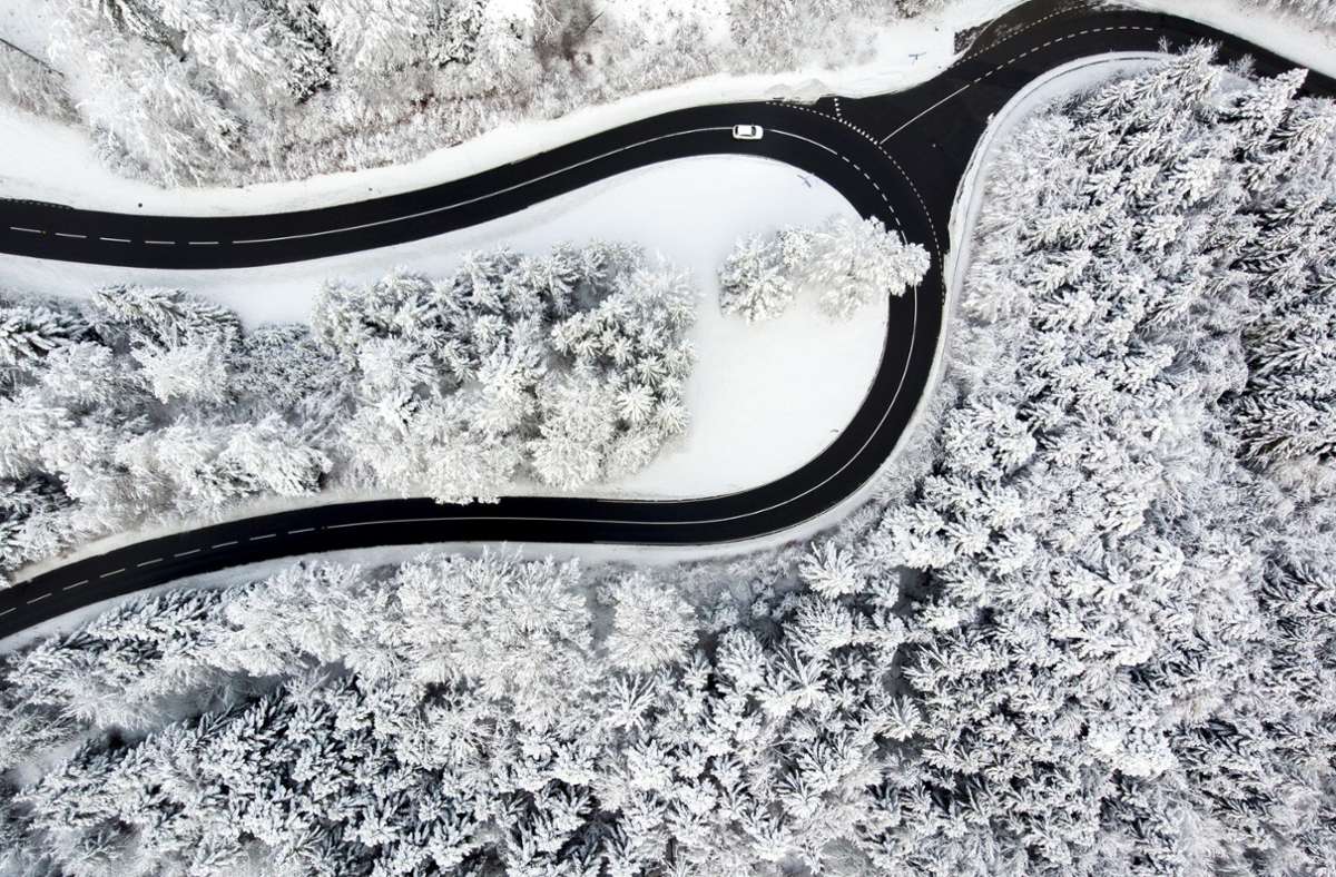 Ein Auto fährt auf der Straße des „Col du Mollendruz“ zwischen schneebedeckten Bäumen eines Waldgebiets.