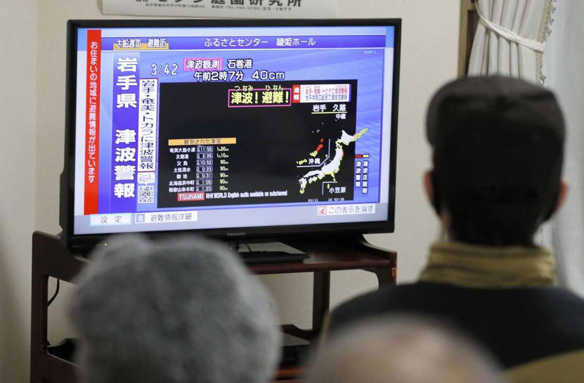 Menschen verfolgen auf einem Bildschirm die Tsunami-Warnungen für die Gebiete an der japanischen Pazifikküste, nachdem sie in einen Tempel evakuiert worden sind.