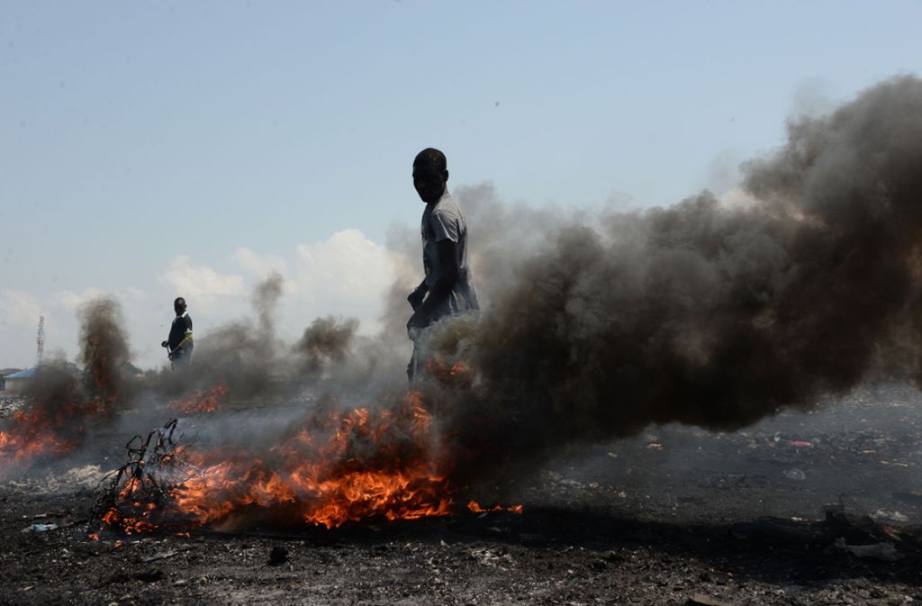 Männer verbrennen auf dem Schrottplatz Agbogbloshie in Accra, Ghana, Kabel und andere Teile alter Elektrogeräte, um die rohen Metalle zu gewinnen und diese weiterzuverkaufen.