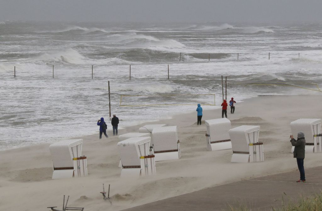 Mehrere Menschen stehen am Dienstag auf Wangerooge bei stürmischem Wetter am Strand.