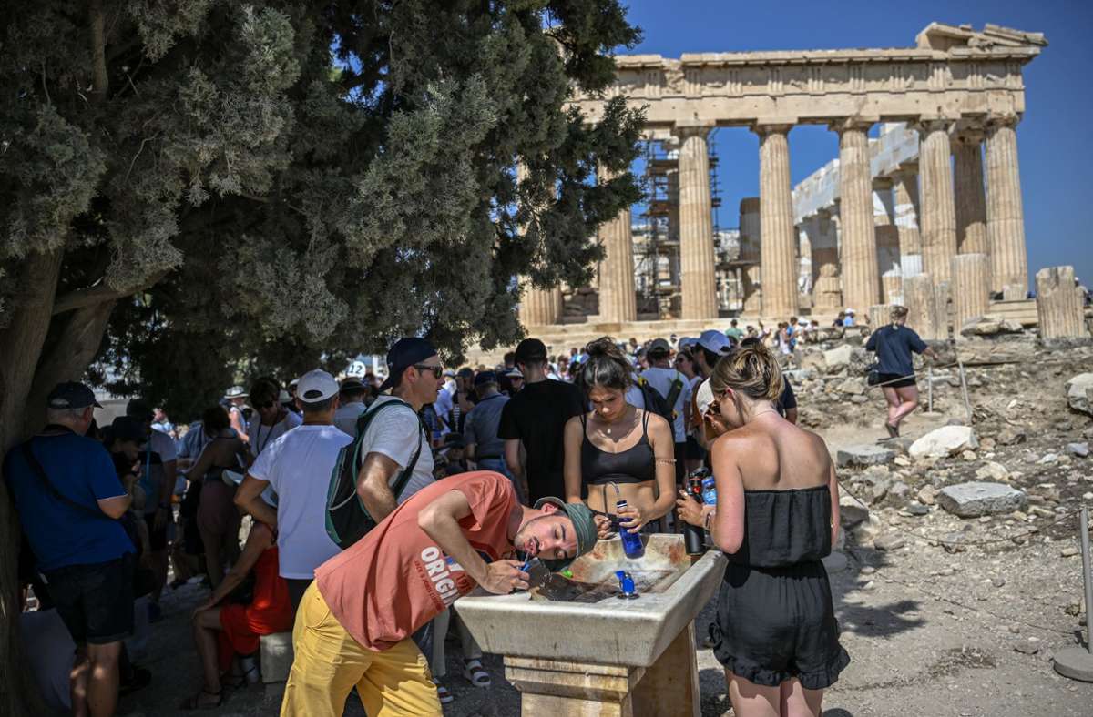 Touristen kühlen sich an einem Wasserspender bei ihrem Besuch des Parthenon-Tempels auf dem Akropolis-Hügel.