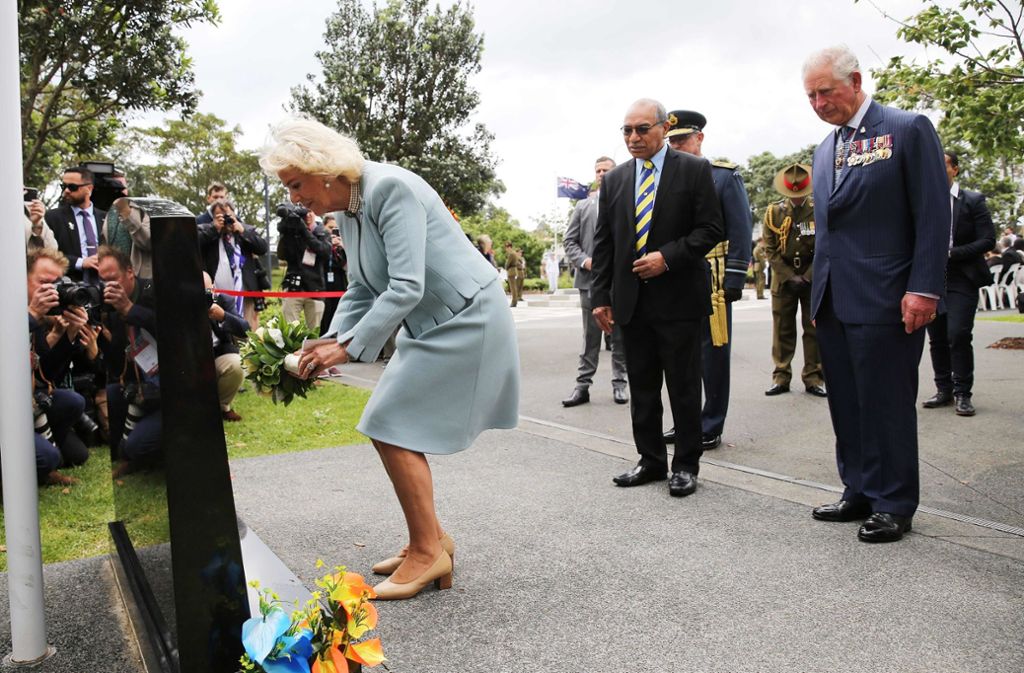 Camilla platziert symbolisch Blumen an einem Grabstein.