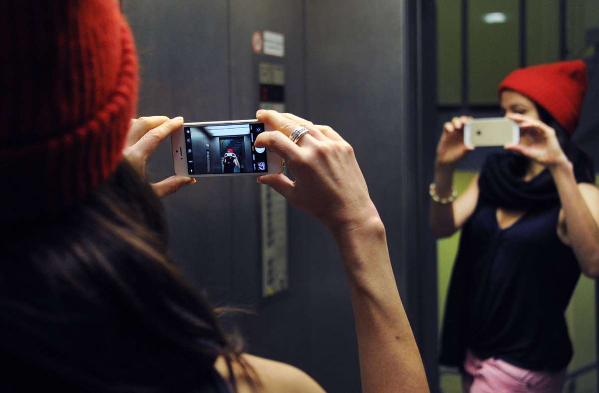 Eine junge Frau macht in einem Aufzug ein Spiegelselfie. Und je mehr Selfies, desto öfter sind die Menschen mit den Fotos unzufrieden oder sehnen sich nach einem Ideal. Experten sagen: Der Selfie-Trend steigert die Nachfrage nach Schönheitsoperationen.