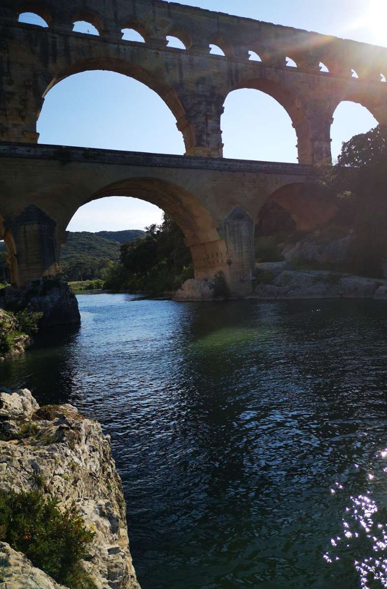 Blick auf das Aquädukt Pont du Gard, das mit seinen drei übereinanderliegenden Arkaden einen Fluss überquert.