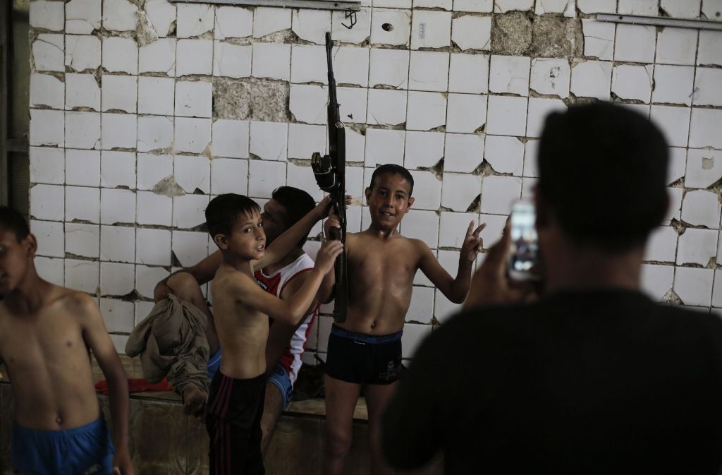 Kinder posieren mit einem Sturmgewehr für ein Foto.