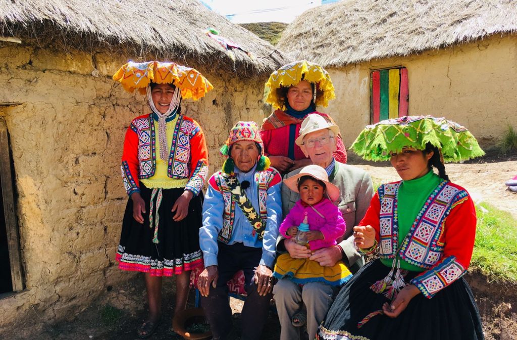 Andenhirte Modesto und Ernst zwischen drei Peruanerinnen auf einer Bank vor einem Lehmhaus mit Strohdach