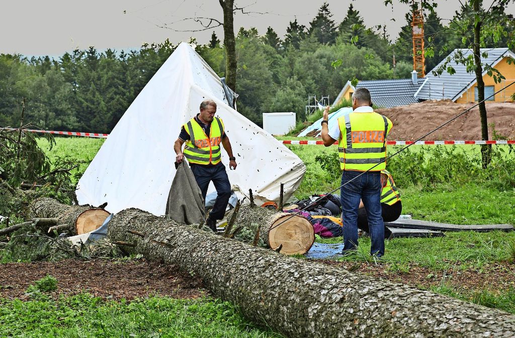 Polizisten untersuchen das beschädigte Zelt, auf das der Baum gestürzt ist. Ein 15-Jähriger wurde bei dem Unglück getötet.