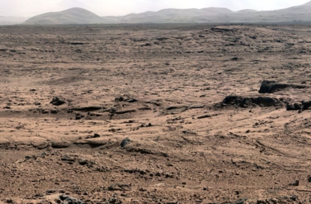 Dieses Panoramafoto hat der Roboter Curiosity im November 2012 geschossen. Die Sonde ist in einem Krater gelandet, in dessen Mitte sich der Mount Sharp erhebt. Im Hintergrund sieht man Ausläufer dieses Berges. Die Farben sind an irdische Verhältnisse angepasst: So würde es aussehen, wenn der Krater auf der Erde wäre.