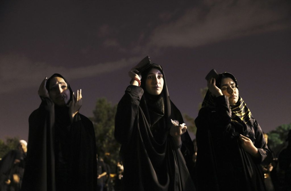 Drei in schwarz gekleidete Frauen in Teheran bedecken ihren Kopf während des Gebets mit dem Koran.