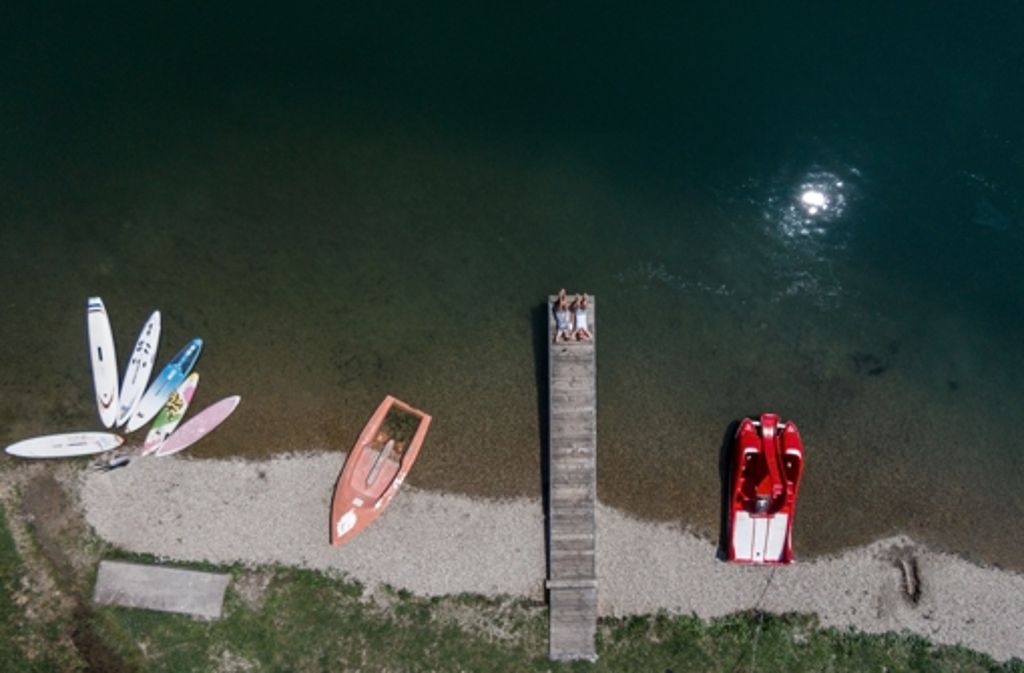 Badegäste liegen am Guggenberger See am Ufer in der Sonne.