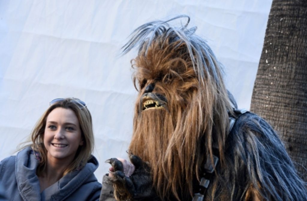 Hand in Hand mit Chewbacca lächelt ein Fan für die Kamera. Chewbacca ist ein Wookiee, dessen Spezies mit einem typisch braunen Fell und einer überdurchschnittliche Größe auffällt.