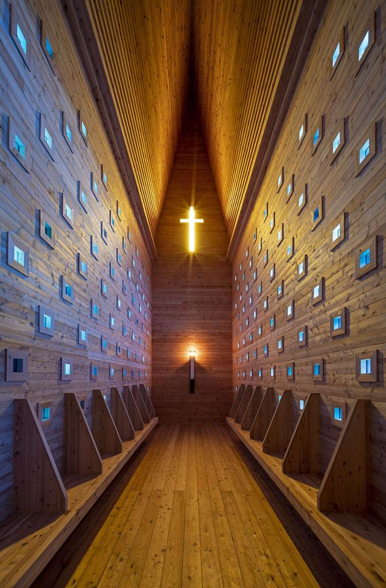 Licht fällt durch 172 quadratische, blau verglaste Öffnungen nach innen. Ein goldgelbes Kreuz durchdringt die nach Westen ausgerichtete Giebelwand der Kapelle bei Oberthürheim.