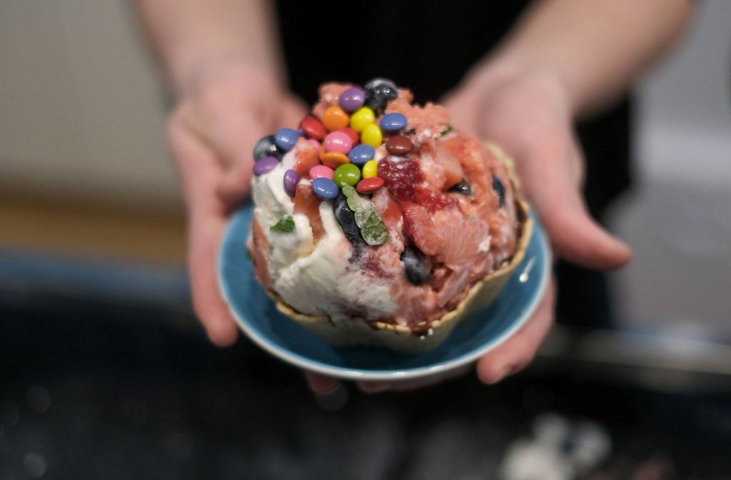Frische Minze, Erdbeeren und Blaubeeren sind in Hamburg in der Eisdiele „Schlecks“ zusammen mit einer Portion Erdbeer- und Joghurteis auf einem kalten Stein zu einer Eiskugel geformt und mit Schokolinsen garniert worden.