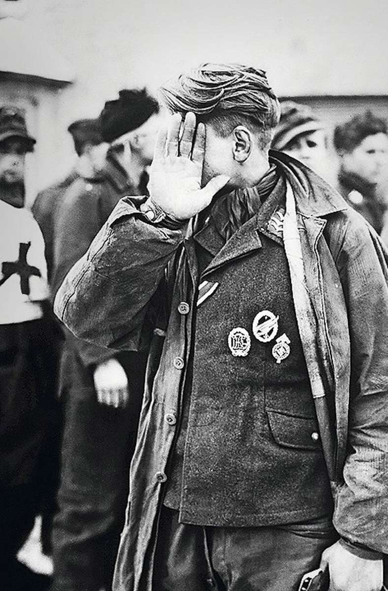Ein gefangener Fallschirmjäger – erkennbar an dem Fallschirmschützenabzeichen auf der Brust – verbirgt Anfang 1945 sein Gesicht.
