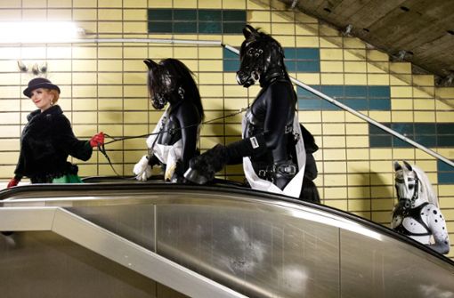 Die Burlesque-Künstlerin Tronicat la Miez fährt am 16. Oktober 2015 in Hamburg mit einer Gruppe Fetisch-Liebhaber – sogenannte „Petplayer“ in Pferde-Outfits – im Rahmen einer Werbeaktion in einem U-Bahnhof eine Rolltreppe hoch. Foto: dpa