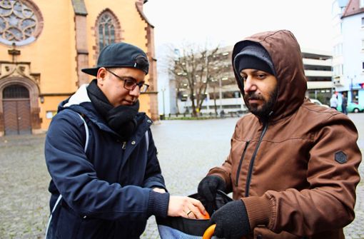 Fatih Ceylan steckt einem Obdachlosen vor der Leonhardskirche eine Orange in den Rucksack. Foto: Tilman Baur