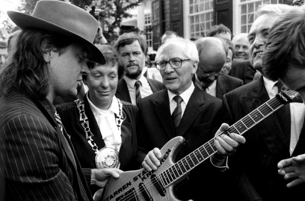 Udo Lindenberg, wie er dem ehemaligen SED-Generalsekretär Erich Honecker (Mitte) bei dessen Besuch 1987 in Wuppertal eine Gitarre mit der Aufschrift „Gitarren statt Knarren“ übereicht.