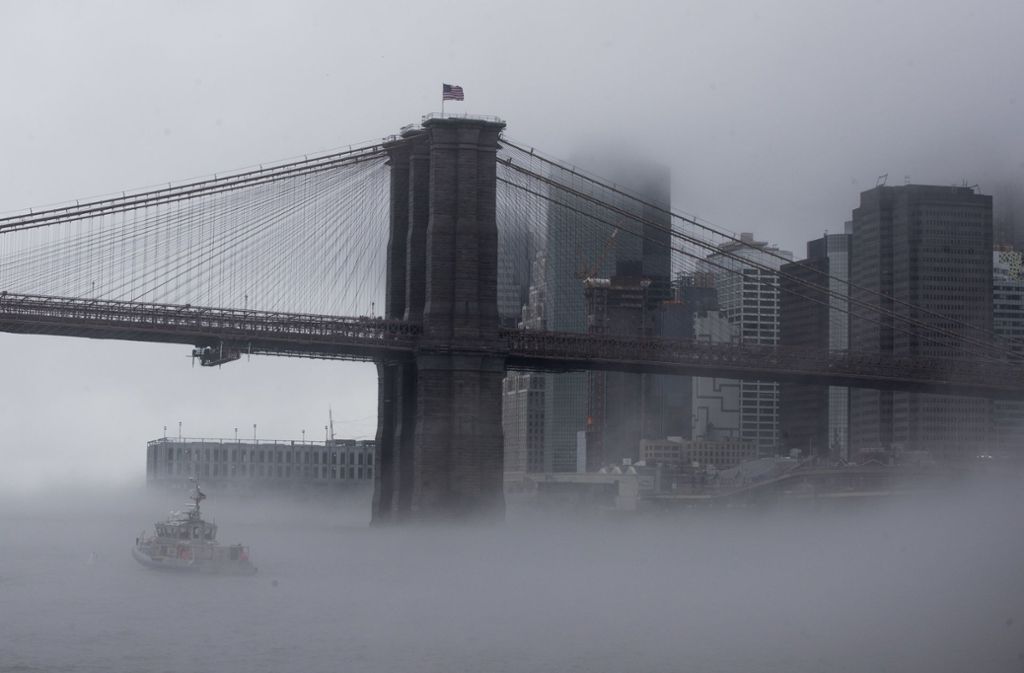 USA, New York: Ein Boot der New Yorker Polizei fährt a unter der Brooklyn Bridge durch den dichten Nebel.