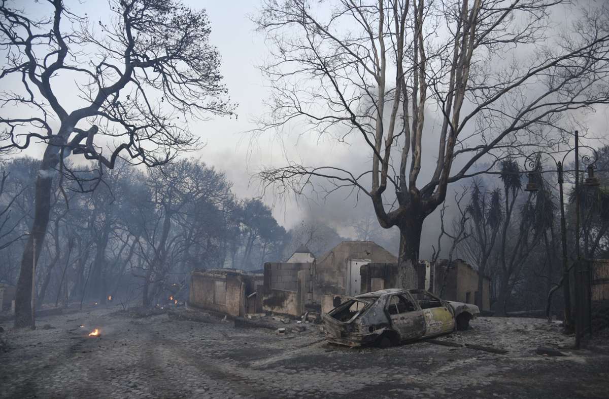 Kleine Flammen brennen neben den verkohlten Überresten eines ausgebrannten Autos und eines Hauses während eines Waldbrandes in der Nähe des Dorfes Lampiri.