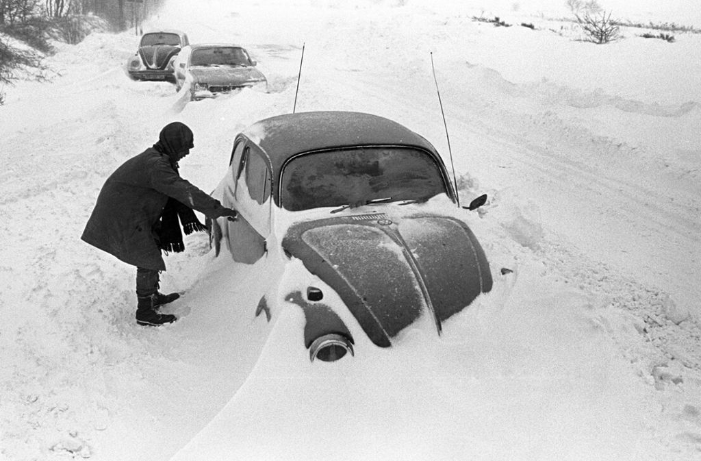 31. Dezember 1978: Ein Autofahrer steht in Cuxhaven neben seinem am Straßenrand im Schnee stecken gebliebenen VW-Käfer.