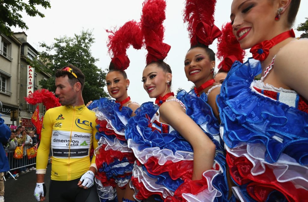 Mark Cavendish im gelben Trikot posiert vor der zweiten Etappe mit Tänzerinnen des Moulin Rouge.