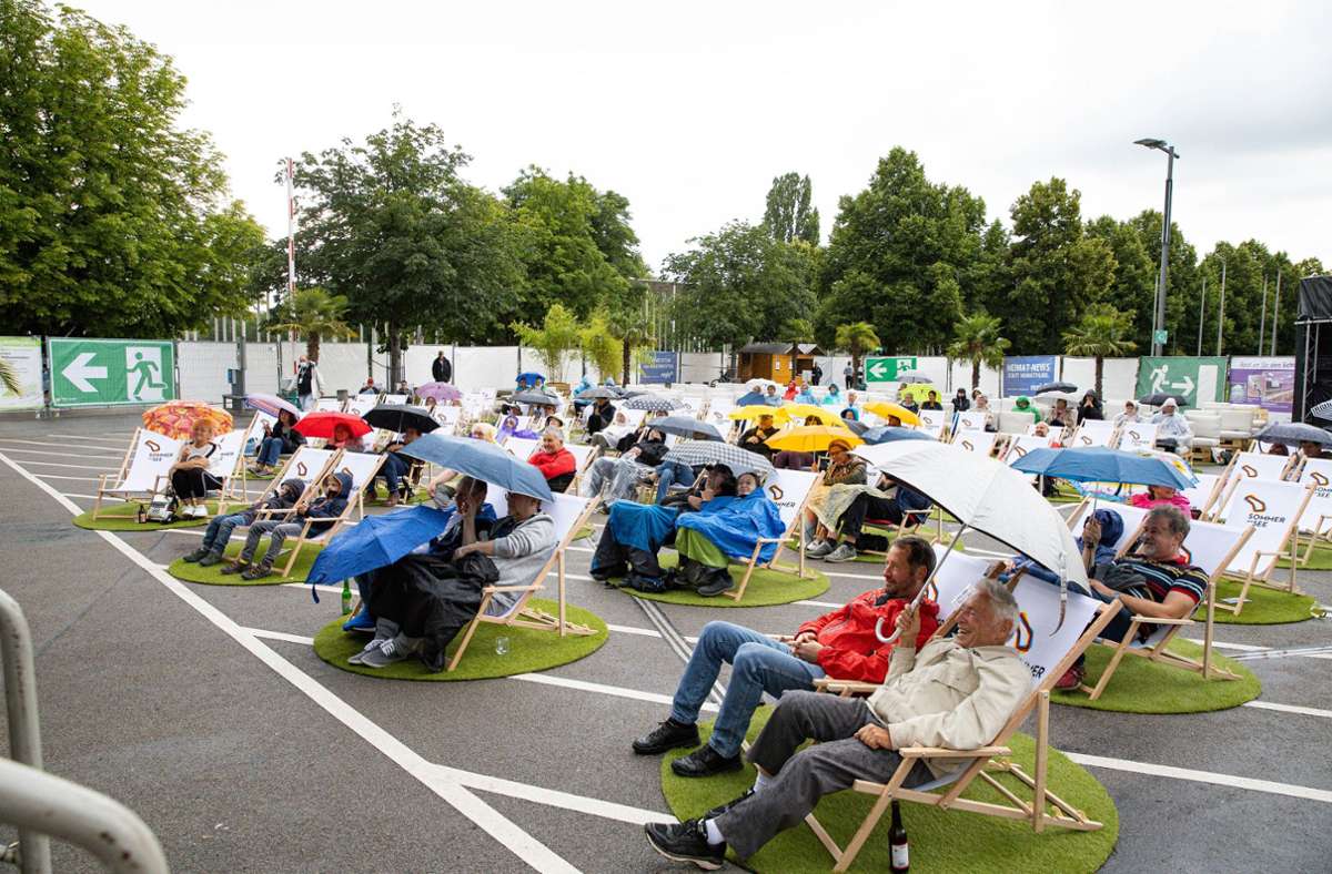 Mit Regenschirm und Plastikponcho sitzen die Zuschauer auf Liegestühlen.