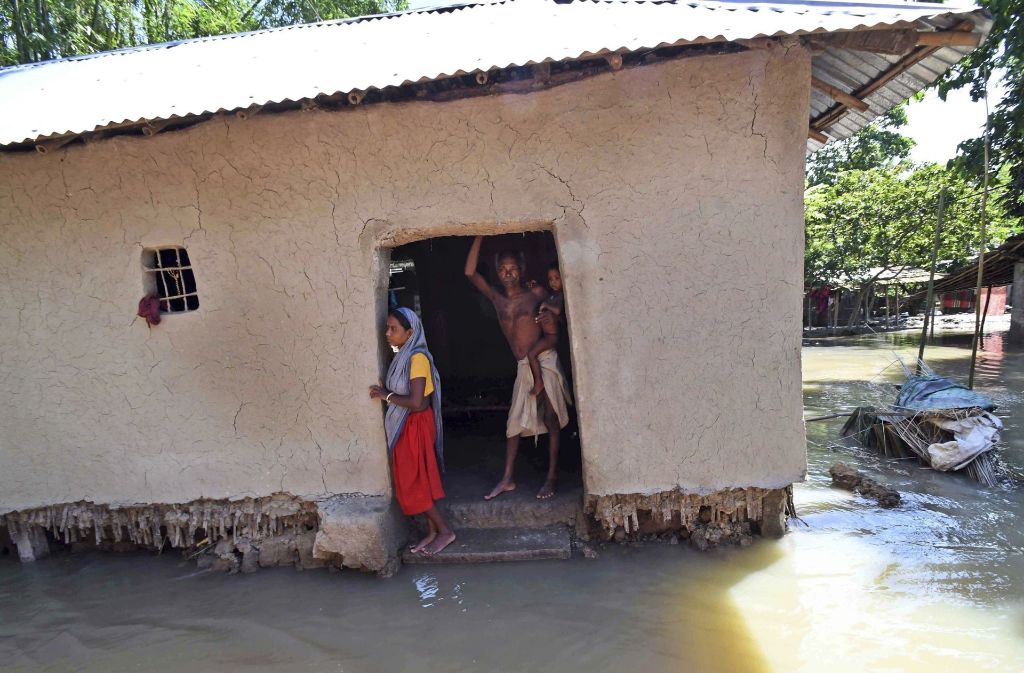 Dorfbewohner stehen in Bihar (Indien) in ihrem überfluteten und zerstörten Haus.