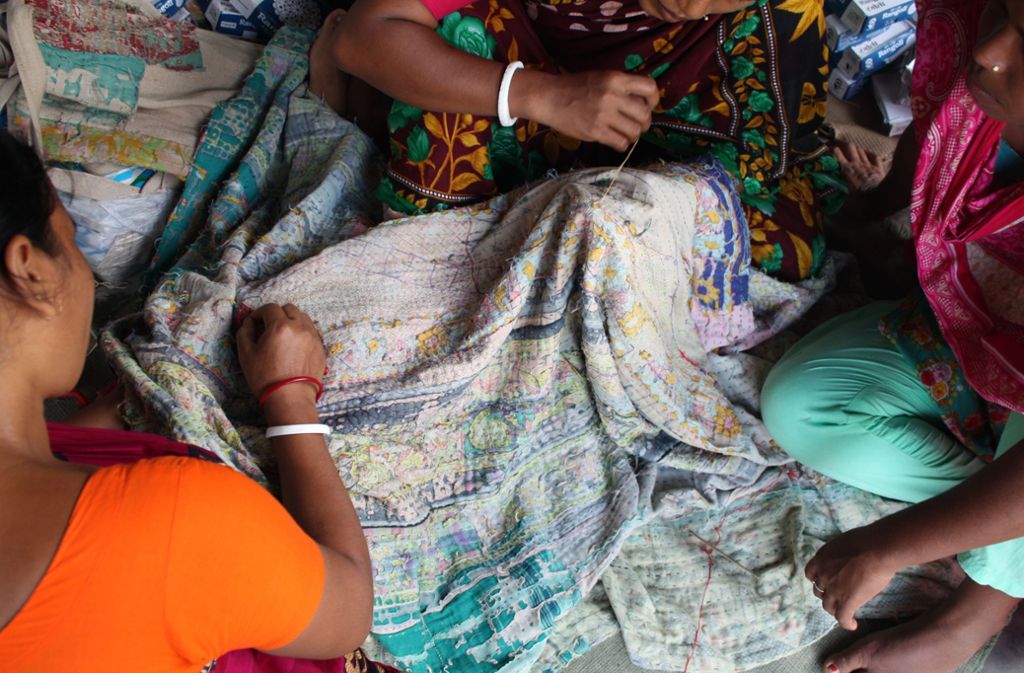 Grundlage der Textilkunst sind zu Decken übereinandergeschichtete Saris. Die Familien schlafen auf den Decken, dadurch wetzt sich die Oberfläche ab. So entstehen lebendige Strukturen, an denen sich Familiengeschichte ablesen lässt.
