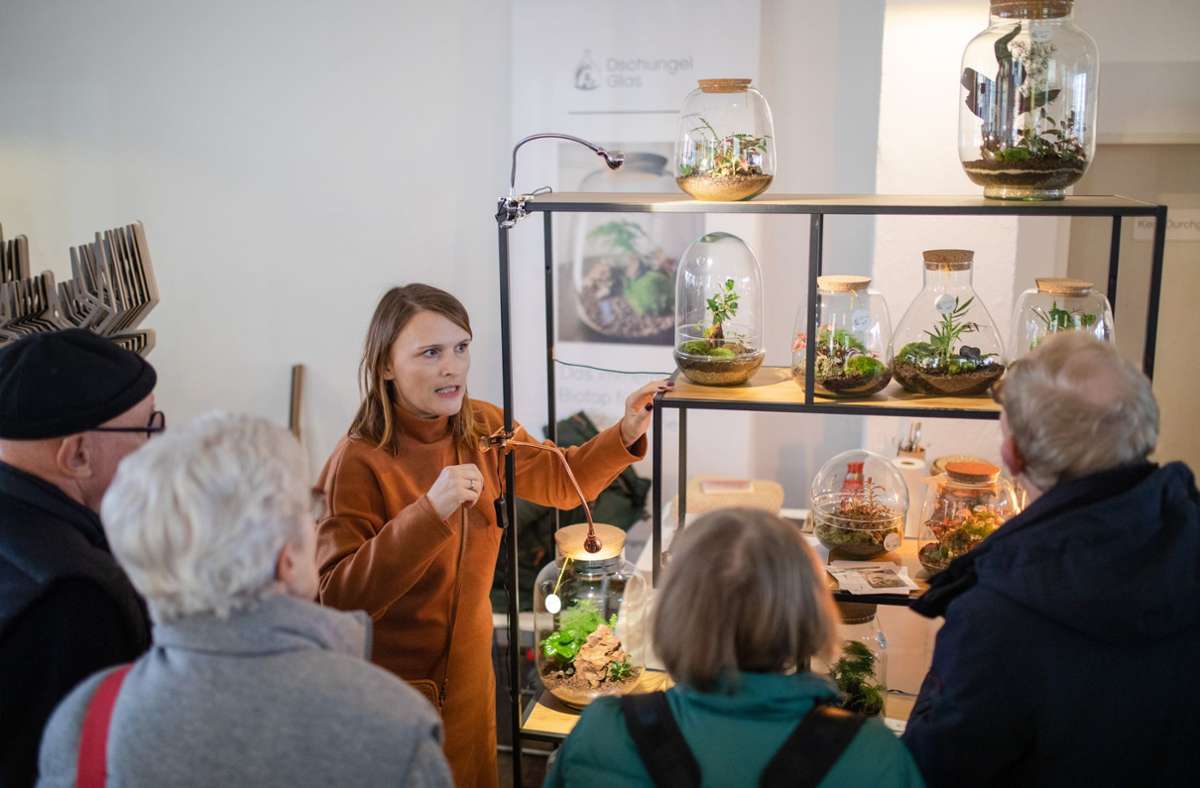 Eine Ausstellerin präsentiert Besuchern ihre Pflanzen im Glas
