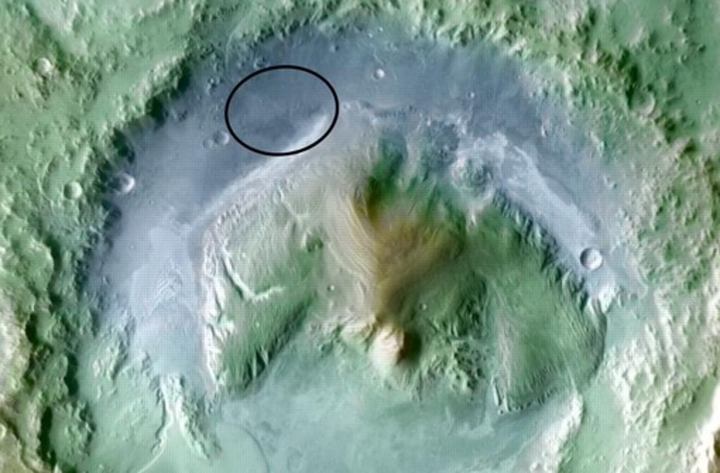 Der Gale-Krater, in dem Curiosity gelandet ist, ist rund 150 Kilometer breit und vor mindestens 3,5 Milliarden Jahren entstanden. Der Kreis zeigt den Bereich an, in dem Curiosity landen sollte. Der Roboter ist tatsächlich ziemlich genau in der Mitte gelandet. Die Farben dieses Bildes sind nicht echt: Sie zeigen die Höhenunterschiede an. Die blauen Regionen liegen tief, die braunen hoch.