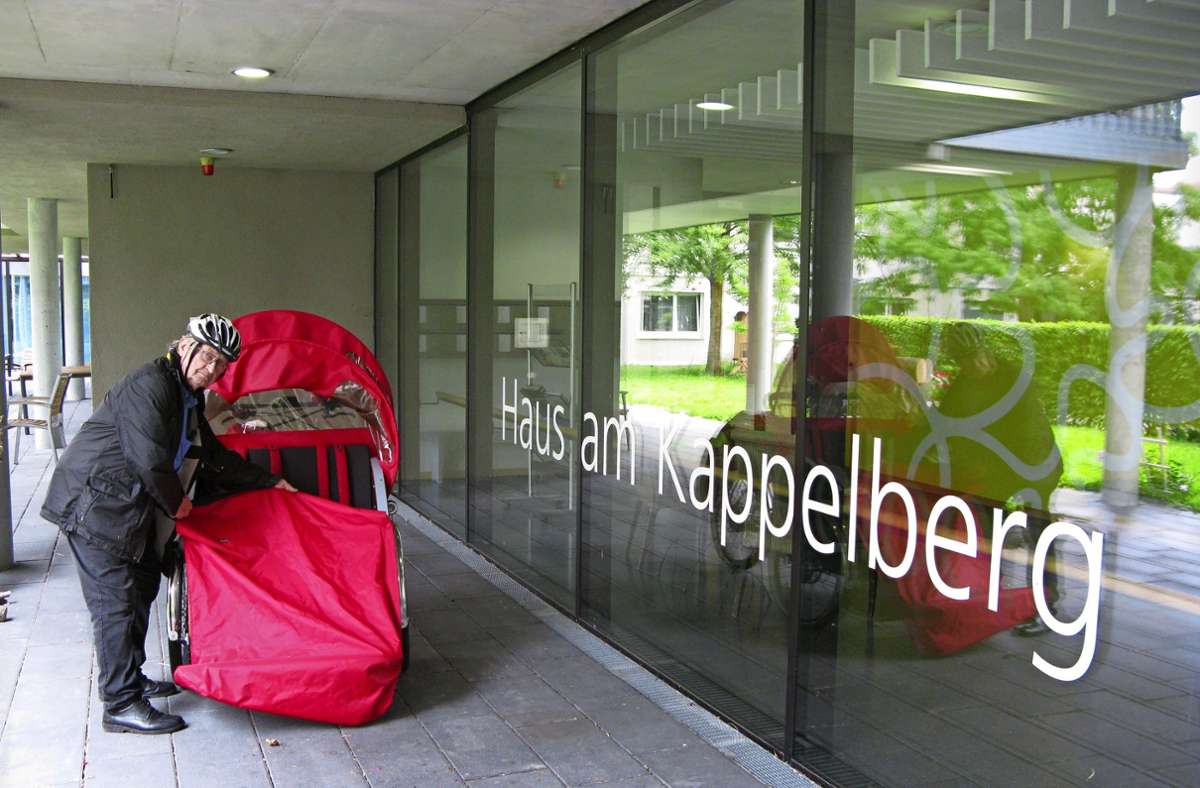 Hermann Werner bereitet die Rikscha vor dem Haus am Kappelberg für die Ausfahrt vor und holt den roten Regenschutz heraus.