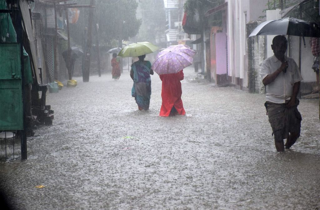 Menschen mit Regenschirmen waten in Balurghat (Indien) durch eine überflutete Straße.