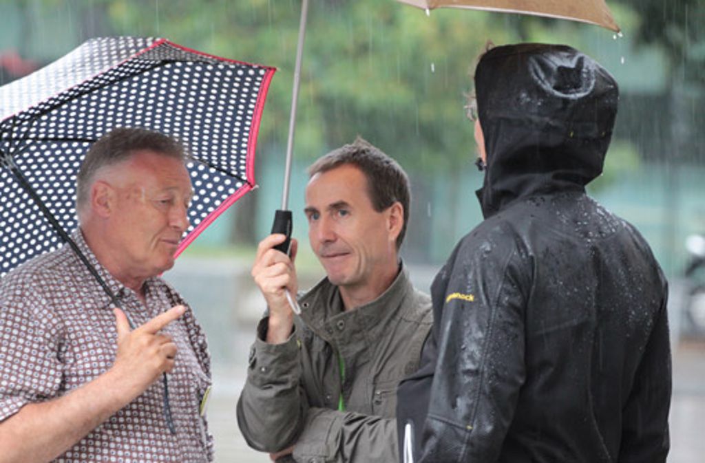 Drei Stuttgarter unterhalten sich bei strömenden Regen vor der Mahnwache.