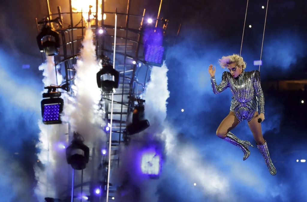 Silberfarbener Glitzeranzug, kniehohe Stiefel, glitzernde Maske um die Augen. Unter Lady Gaga, die sich am Lüftungsschacht auf dem Dach einer Sportarena in Houston postiert hat, warten die Football-Fans auf ihre Halbzeitshow beim Super Bowl.