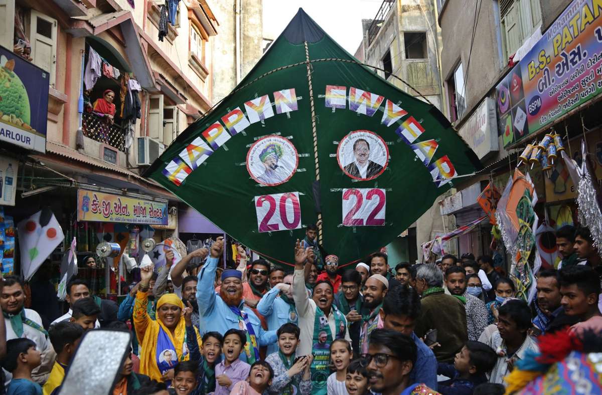 Indien, Ahmedabad: Mitglieder einer politischen Partei stehen auf einer Straße und feiern gemeinsam mit anderen Personen am Silvesterabend das neue Jahr unter einem Drachen, auf dem «Frohes Neues Jahr» zu lesen ist.