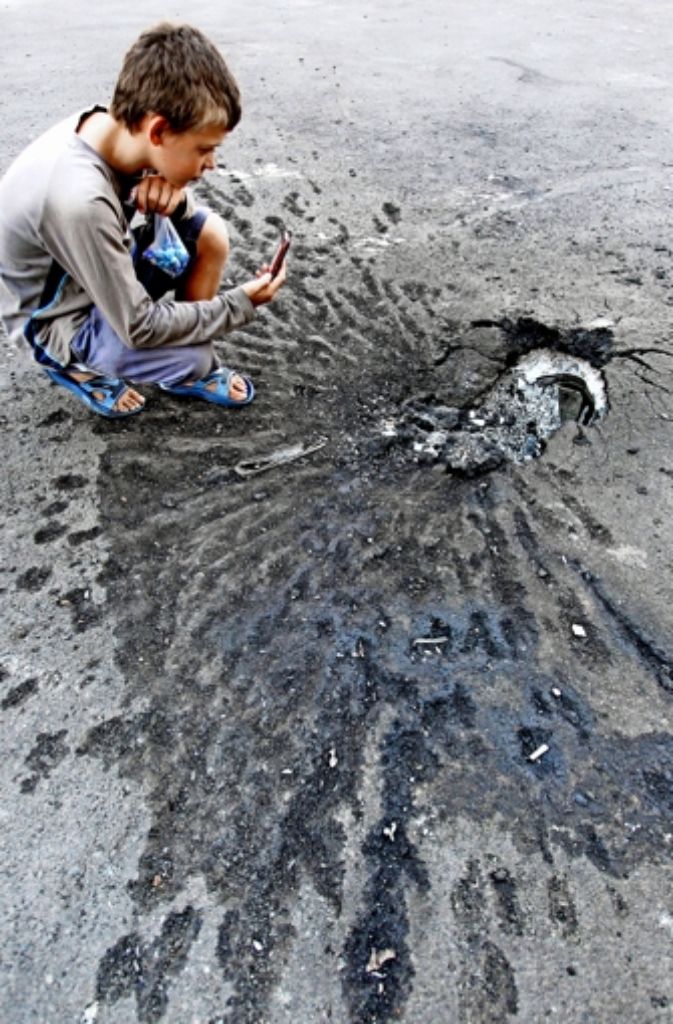 Ein Junge fotografiert Spuren eines Granateinschlags in Donezk. Foto: dpa