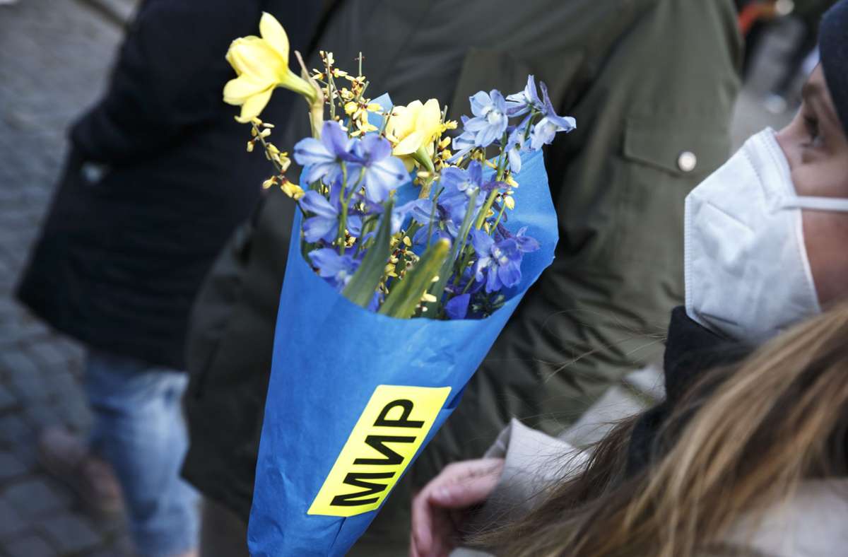 Bei der Kundgebung der Friedensbewegung an der Planie hält eine Frau Blumen in den Farben der Ukraine. Auf der Verpackung steht das russische und ukrainische Wort für Frieden.