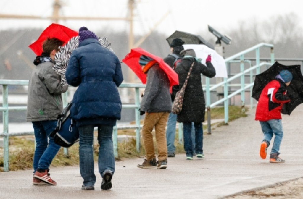 Spaziergänger mit Regenschirmen kämpfen in Lübeck-Travemünde (Schleswig-Holstein) mit Windböen.