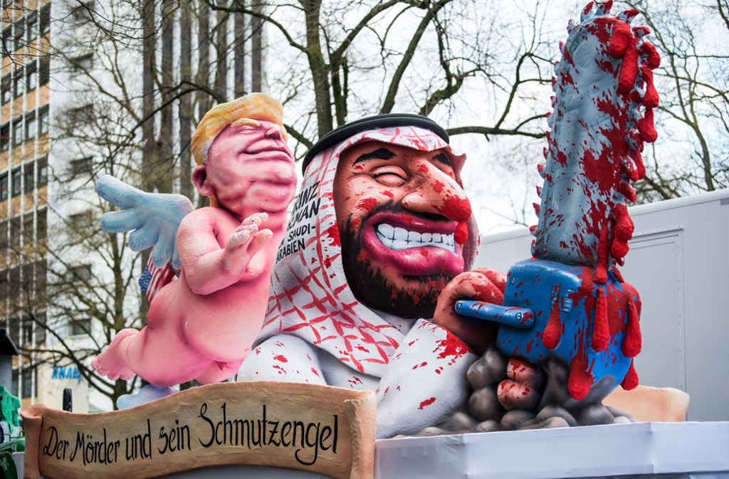 Düsseldorfs Karnevalisten zeigen den US-Präsidenten als nackigen „Schmutzengel“, der seine schützende Hand über einen mit blutiger Kettensäge ausgestatteten Prinz Salman von Saudi-Arabien hält.