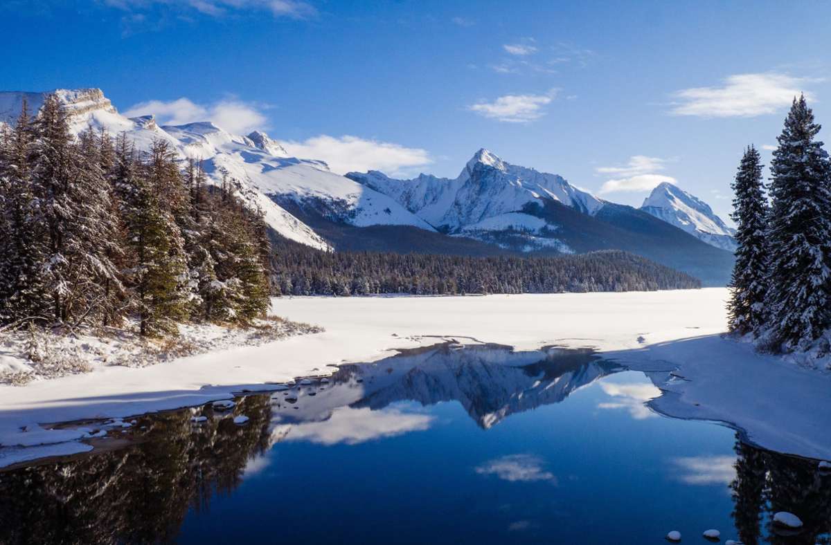 Die schneebedeckten Gipfel der kanadischen Rocky Mountains spiegeln sich im ruhigen Wasser.