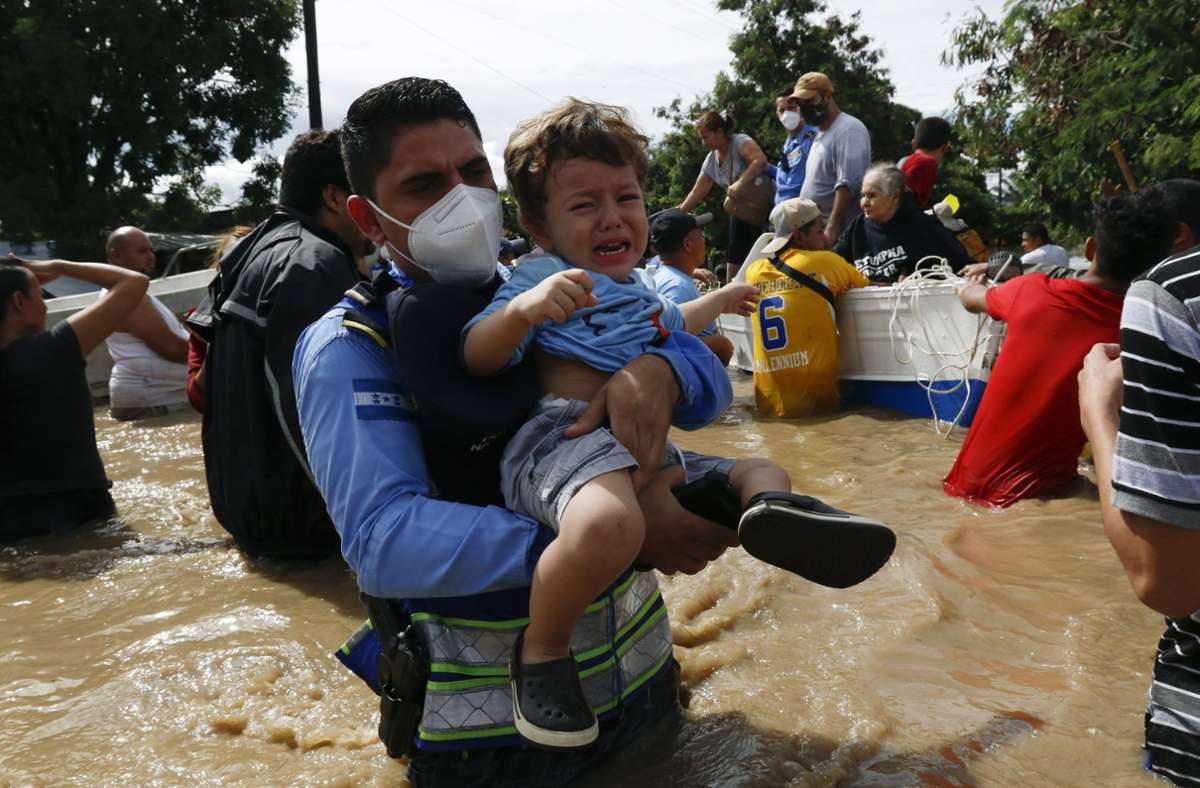 Tropensturm in Honduras: Ein Polizist trägt ein Kind durch eine überflutete Straße
