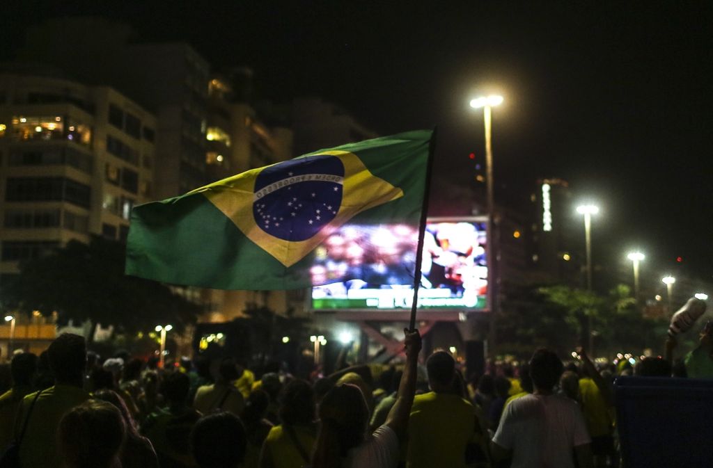 Eine brasilianische Fahne weht, im Hintergrund die Live-Übertragung der Parlamentswahl.