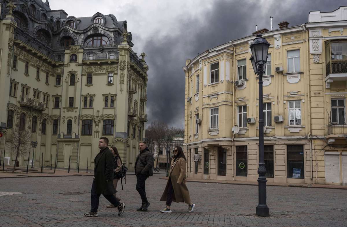 Ukraine, Odessa: Eine Gruppe von Menschen geht auf einer Straße. Am Horizont steigt nach den Beschuss des russischen Militärs schwarzer Rauch auf.