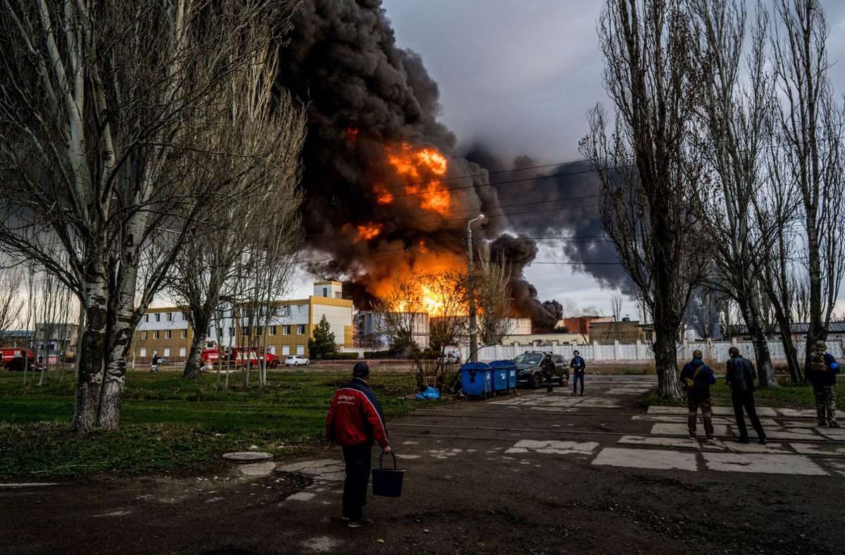 Ukraine, Odessa: Personen stehen auf einer Straße und beobachten wie am Horizont Feuer und schwarzer Rauch aufsteigt, nachdem das russische Militär ein Treibstoffdepot beschossen hat.
