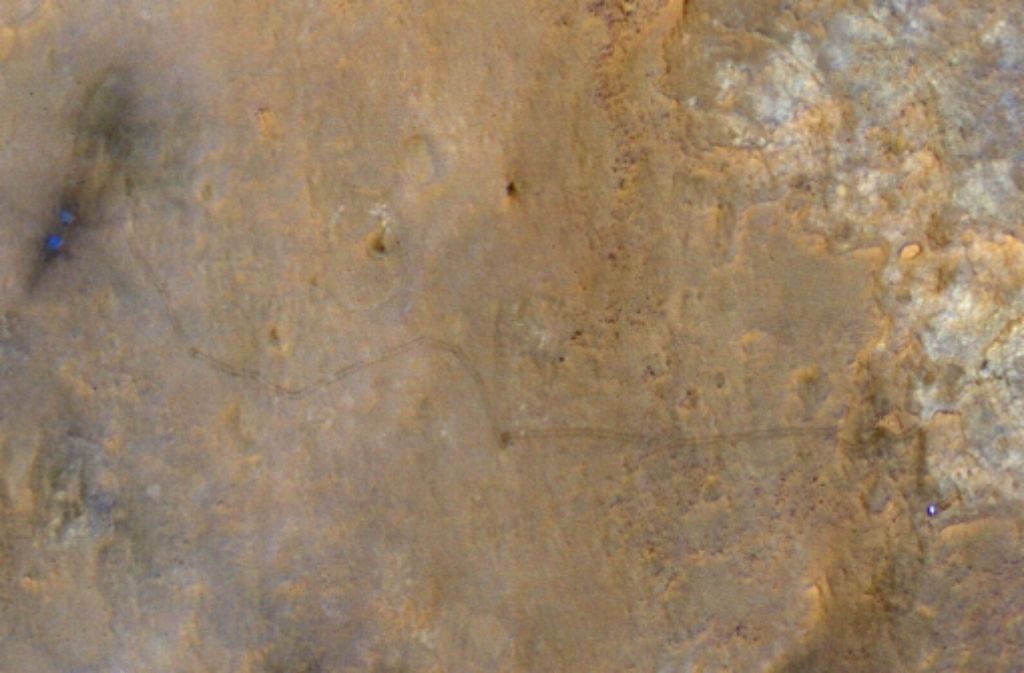 Man muss schon genau hinsehen, um die Fahrspur zu erkennen, die Curiosity im Sand hinterlassen hat. Die Fahrt beginnt links im Bild, wo dunkle Flecken die Stellen zeigen, an denen die Landeraketen den roten Staub weggeblasen haben. Die Fahrspur ist etwa drei Meter breit. Aufgenommen hat das Bild der US-Satellit „Mars Reconnaissance Orbiter“.
