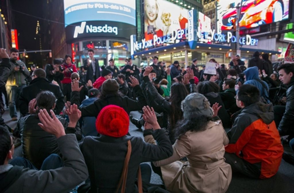 Am Time Square in New York demonstrieren Menschen im Sitzen mit erhobenen Händen.